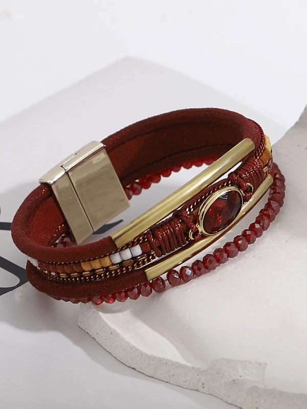 Czerwona bransoletka z wieloma warstwami, ozdobiona złotymi elementami, fasetowanymi koralikami i centralnym czerwonym kamieniem w owalnej oprawie.