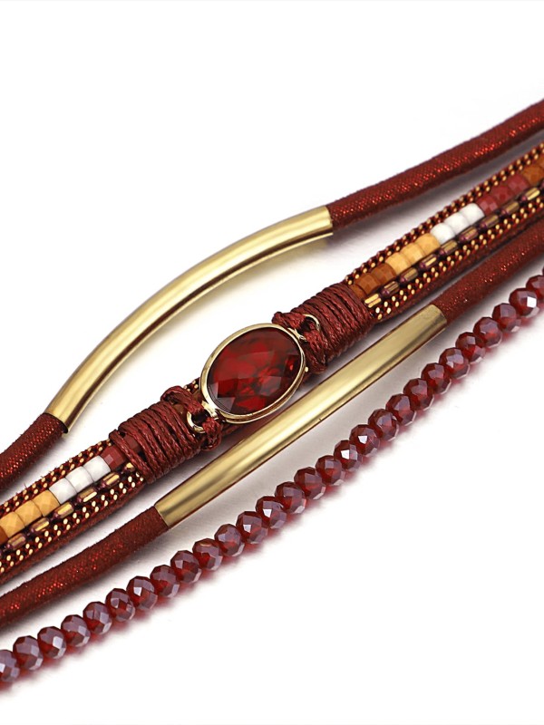 Czerwona bransoletka z wieloma warstwami, ozdobiona złotymi elementami, fasetowanymi koralikami i centralnym czerwonym kamieniem w owalnej oprawie.
