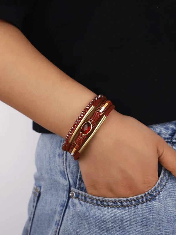 Czerwona bransoletka z wieloma warstwami, ozdobiona złotymi elementami, fasetowanymi koralikami i centralnym czerwonym kamieniem w owalnej oprawie.