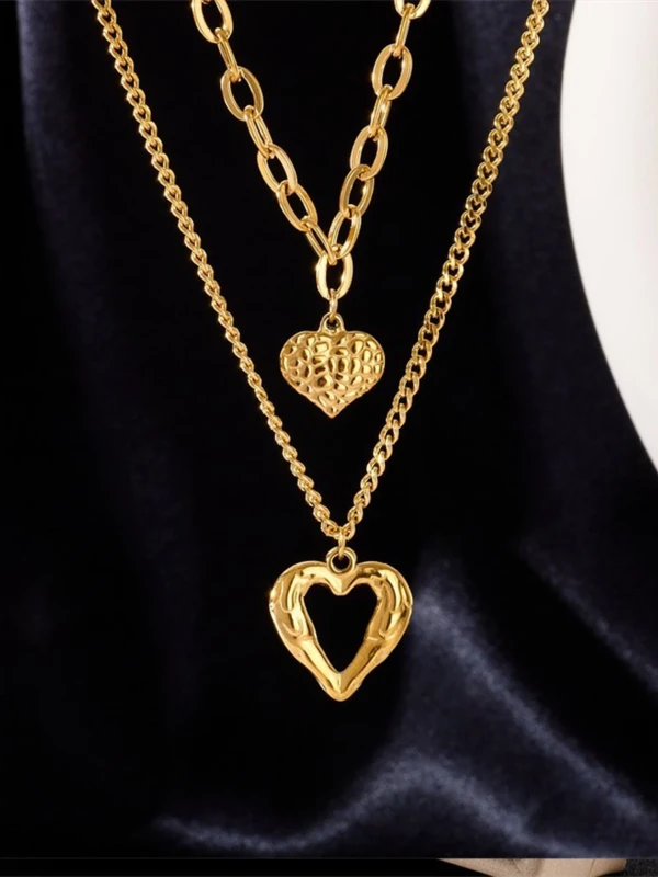 Podwójny naszyjnik w kolorze złotym z dwoma różnymi łańcuszkami; na krótszym zawieszka w formie złotego serduszka o młotkowanej fakturze, na dłuższym ażurowe serce o organicznym kształcie.