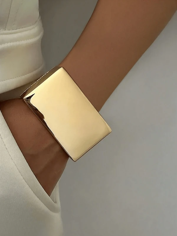 Szeroka złota bransoletka typu cuff o gładkiej, lustrzanej powierzchni na nadgarstku (4).webp