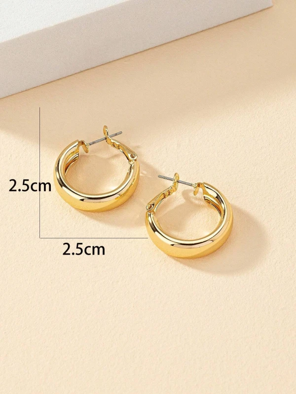 Złote kolczyki koła Golden Glow o gładkiej, wypukłej formie i średnicy około 2,5 cm, pokazane na uchu oraz na jasnym tle (1).webp