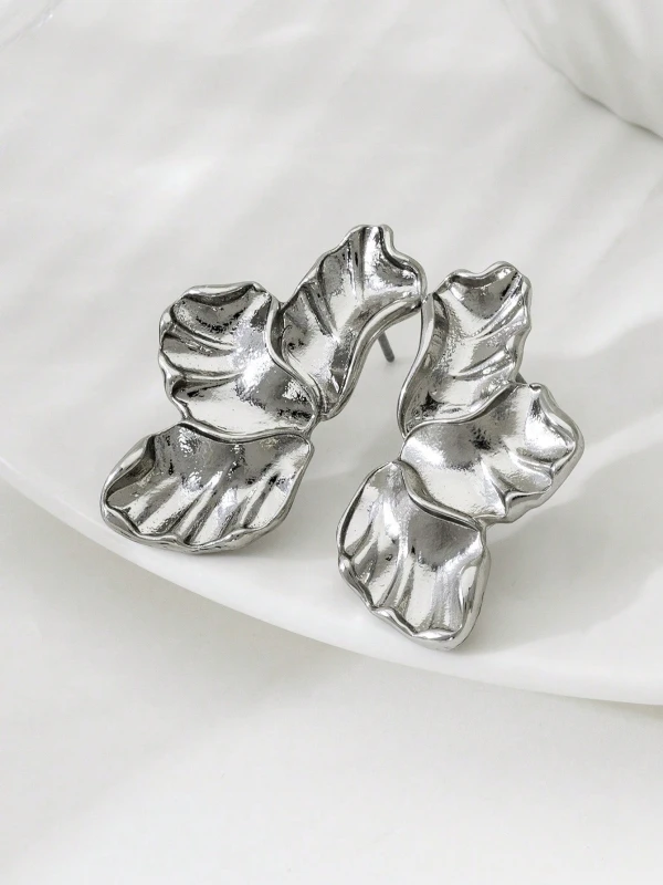 Srebrne kolczyki Silver Petals w formie trzech nieregularnych, rzeźbionych listków lub płatków, pokazane na uchu i na jasnym tle (5).webp