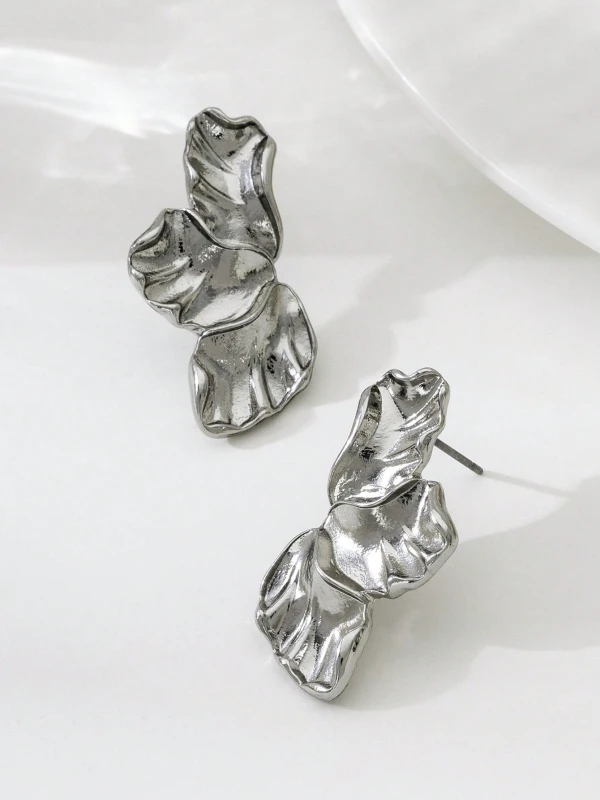 Srebrne kolczyki Silver Petals w formie trzech nieregularnych, rzeźbionych listków lub płatków, pokazane na uchu i na jasnym tle (4).webp
