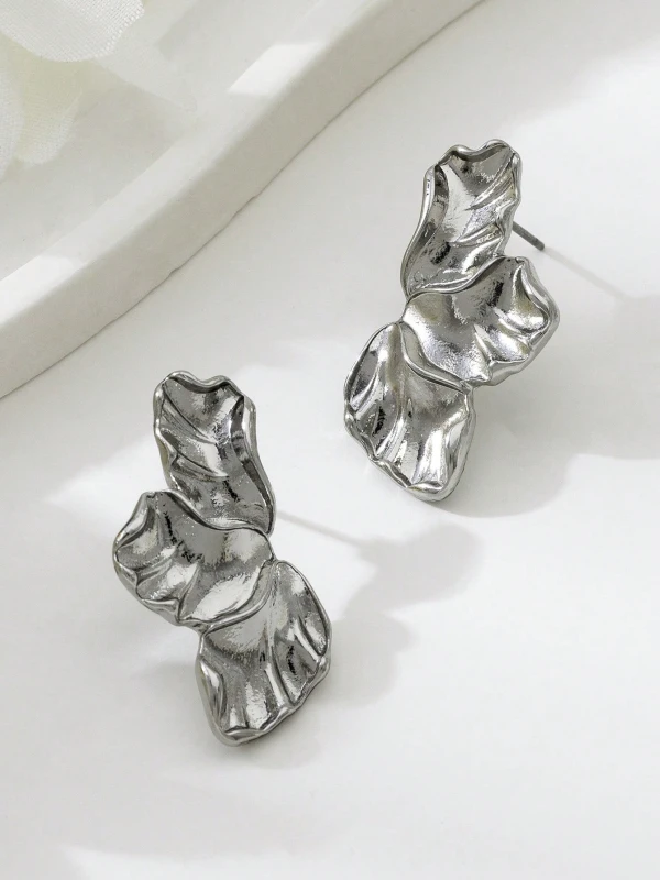 Srebrne kolczyki Silver Petals w formie trzech nieregularnych, rzeźbionych listków lub płatków, pokazane na uchu i na jasnym tle (2).webp