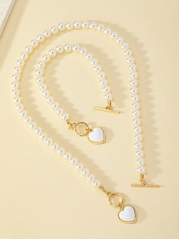 Zestaw biżuterii Pearl Heart z perłowym naszyjnikiem i bransoletką, ozdobiony złotymi zapięciami typu toggle oraz białymi zawieszkami w kształcie serca w złotej oprawie (1).webp