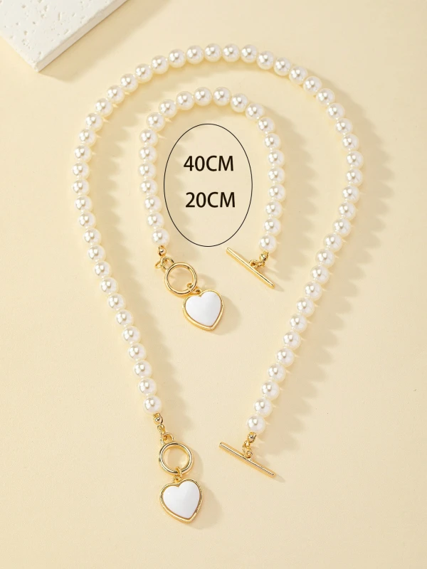 Zestaw biżuterii Pearl Heart z perłowym naszyjnikiem i bransoletką, ozdobiony złotymi zapięciami typu toggle oraz białymi zawieszkami w kształcie serca w złotej oprawie (3).webp