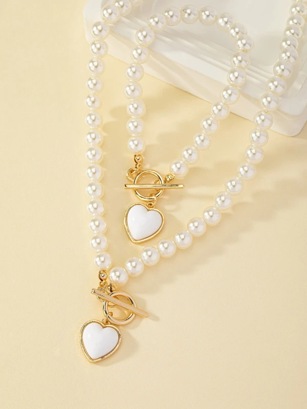 Zestaw biżuterii Pearl Heart z perłowym naszyjnikiem i bransoletką, ozdobiony złotymi zapięciami typu toggle oraz białymi zawieszkami w kształcie serca w złotej oprawie (4).webp
