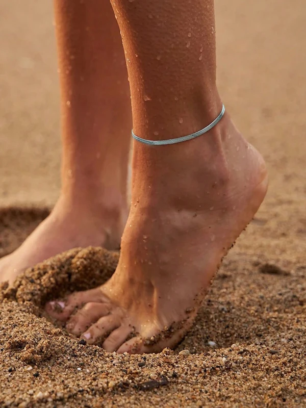Podwójna srebrna bransoletka na nogę z cienkim łańcuszkiem i płaskim paskiem, pokazana na kostce na plaży oraz na ciemnym tle z wymiarem 20+5 cm (4).webp